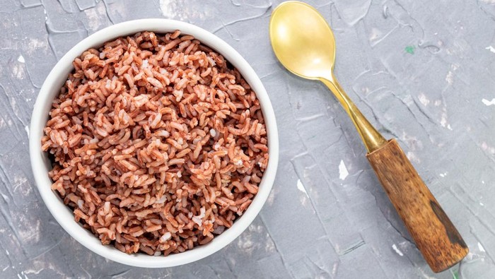 Rice red in bowl isolated on blue grey background has spoon close up, top view, Asian food and drink concept.