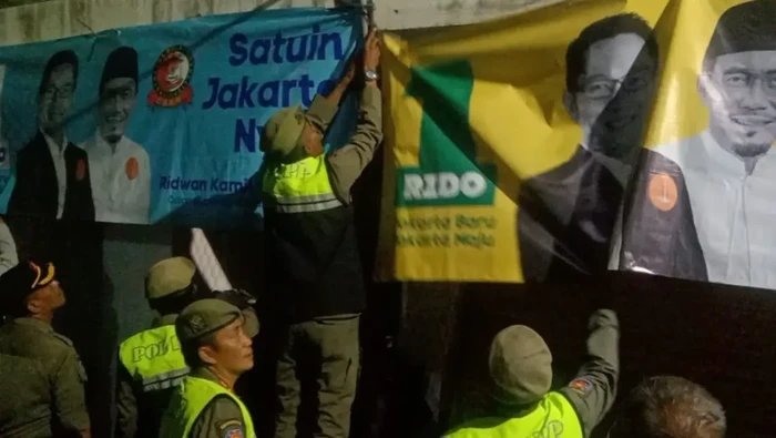 Petugas gabungan dari berbagai unsur menurunkan alat peraga kampanye (APK) di Jakarta pada masa tenang Pilkada 2024. Petugas mencopot spanduk hingga baliho. (Antara)