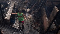 Seorang anak tampak berjalan di antara puing rumah yang hancur akibat kebakaran.
