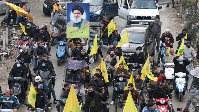 Simpatisan Hizbullah Rayakan Gencatan Senjata dengan Israel Men carry Hezbollah flags and a picture depicting late Hezbollah leader Sayyed Hassan Nasrallah, as they drive past damaged buildings at the entrance of Beirut's southern suburbs, after a ceasefire between Israel and Hezbollah took effect, Lebanon November 27, 2024. REUTERS/Mohamed Azakir TPX IMAGES OF THE DAY