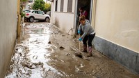 Warga membersihkan lumpur di jalan usai banjir reda.