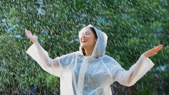 Rainy day asian woman wearing a raincoat outdoors. She is happy.