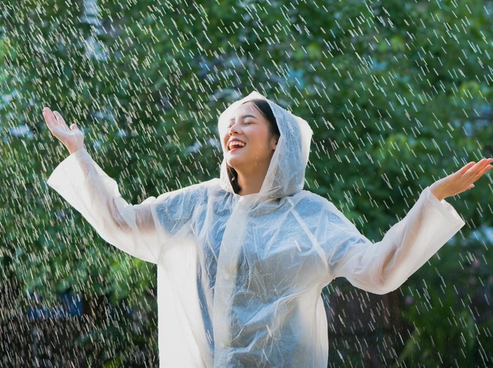 Rainy day asian woman wearing a raincoat outdoors. She is happy.