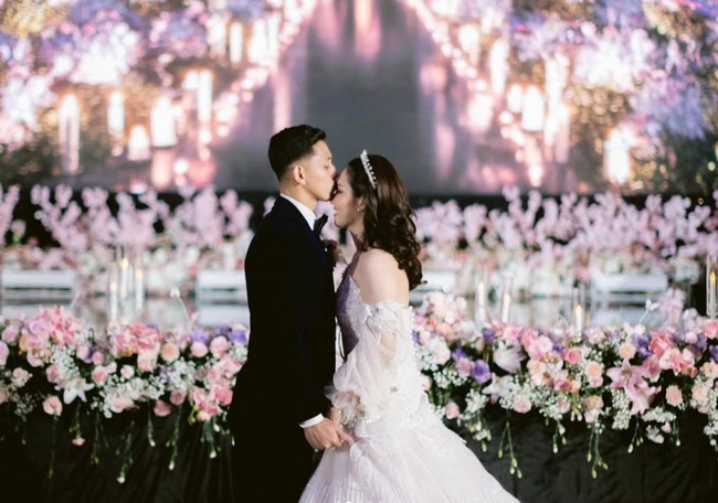 Berbeda dengan akad nikah yang mengusung tema tradisional, resepsi Rian dan Ribka bergaya internasional. Rian tampil gagah mengenakan jas navy berbahan velvet dilengkapi dasi kupu-kupu, sementara Ribka tampil bak princess dengan gaun pengantin putih. Foto: Instagram/@ribkasugiarto