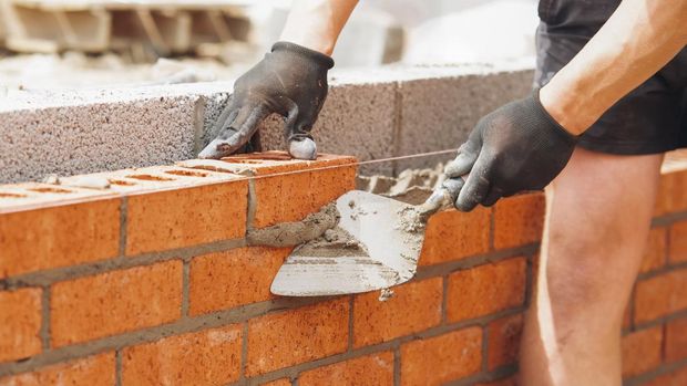 hands of Bricklayer with Masonry Trowel laying bricks on mortar