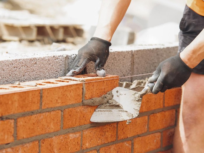 hands of Bricklayer with Masonry Trowel laying bricks on mortar