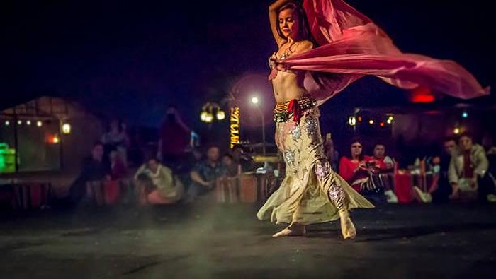 Dubaï, United Arab Emirates - March 28, 2014: In the desert of Duai, a young belly dancer cought in action with spectators all around the stage who enjoy the spectacle.  This show ends wonderfully beautiful day in the desert dubai.