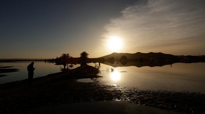 Potret Gurun Sahara yang Masih Terendam Banjir A man stands near sand dunes and palm trees partially covered by floodwaters, after rare rainfall hit the area last September, at sunrise in Merzouga, Morocco December 5, 2024. REUTERS/Darrin Zammit Lupi