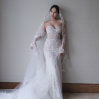 Veil panjang dengan ujung renda menambah kesan dramatis dan romantis, sementara aksen renda pada lengan menambah kesan anggun sekaligus berani. Gaun ini cocok untuk mempelai yang ingin tampil glamor namun tetap menonjolkan sentuhan personal di hari istimewanya. Foto: Instagram