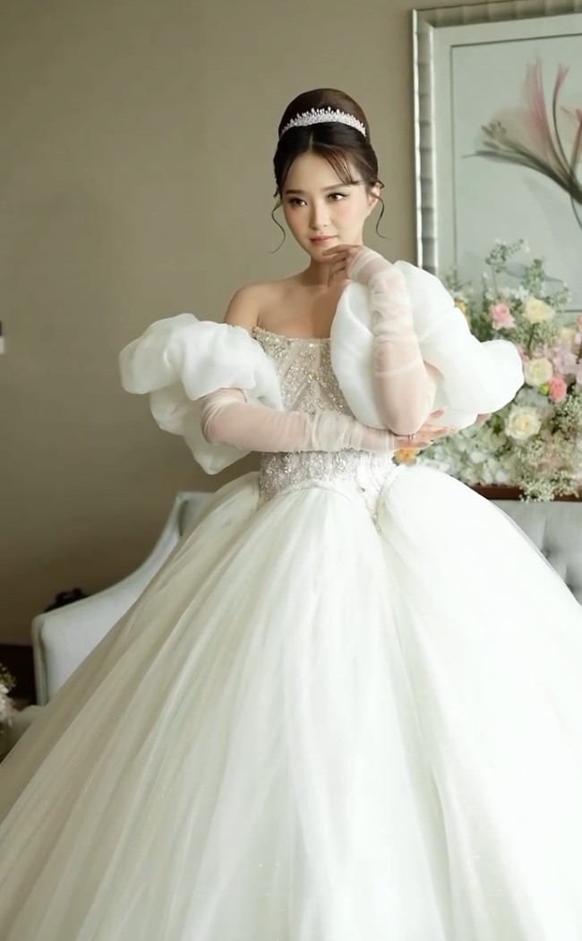 Bagian torso dihiasi detail kristal  an sulaman rumit yang menonjolkan nuansa elegan dan mewah. Lengan puff off-shoulder dengan material transparan menciptakan kesan romantis dan lembut, dilengkapi dengan sarung tangan sheer panjang yang memberi sentuhan vintage. Foto: Instagram