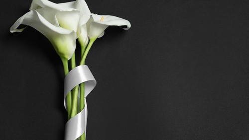 Beautiful calla lilies and white ribbon on black background, flat lay with space for text. Funeral symbol