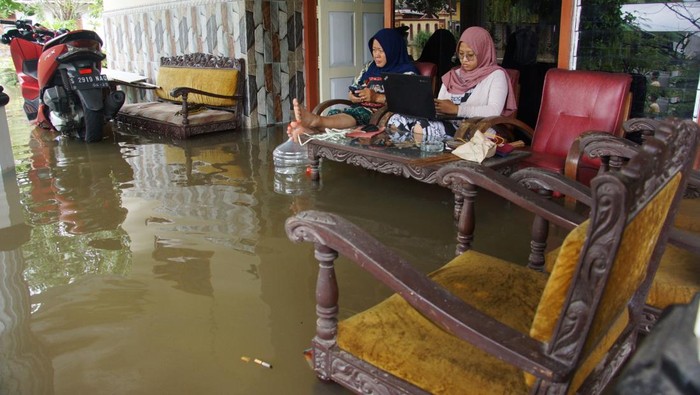 Warga duduk di teras rumah sambil bekerja saat banjir mengenangi Dusun Beluk, Desa Jombok, Kecamatan Kesamben, Kabupaten Jombang, Jawa Timur, Senin (9/12/2024). Dari data BPBD Kabupaten Jombang, banjir akibat luapan sungai Afvour Watudakon itu merendam ratusan rumah dengan ketinggian bervariasi mulai 30 sentimeter hingga 60 sentimeter, selain itu sebanyak 600 jiwa terdampak serta 55 orang mengungsi ke tempat aman. ANTARA FOTO/Syaiful Arif/foc.