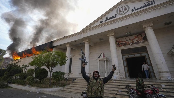 Opposition fighters celebrate as they burn down a military court in Damascus, Syria, Sunday, Dec. 8, 2024. (AP Photo/Hussein Malla)