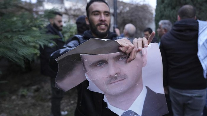 A man tears up a photo of Syrian President Bashar Assad in front of the Syrian embassy in Belgrade, Serbia, Sunday, Dec. 8, 2024. (AP Photo/Darko Vojinovic)