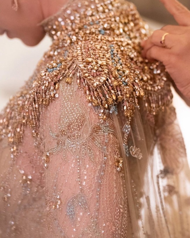 Gaun lace sarat akan detail dengan penekanan pada bagian leher dan dada yang dipenuhi rangkaian payet, kristal serta sequin. Aksen cape panjang menerawang menambah kesan dramatis. Foto: Instagram/@leonardiwedding @itsfrankywu