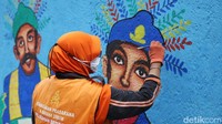 Seorang petugas PPSU menyelesaikan pembuatan mural Ondel-ondel.