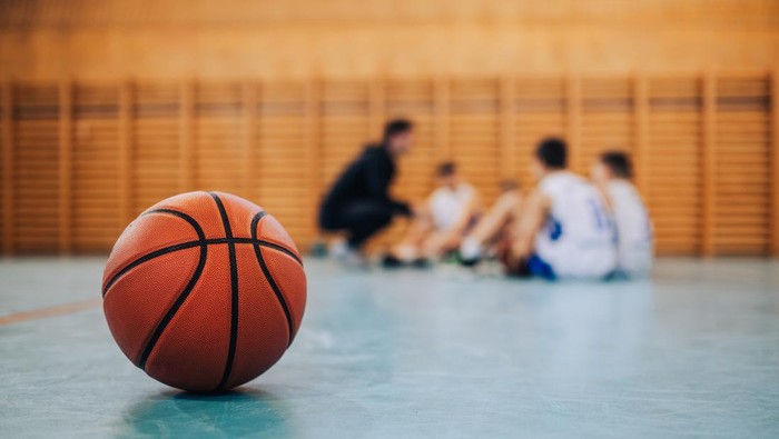 A basketball on court with a junior team with coach in a blurry background. A ball on basketball court during the training. A junior team with basketball coach in a blurry background. Copy space.