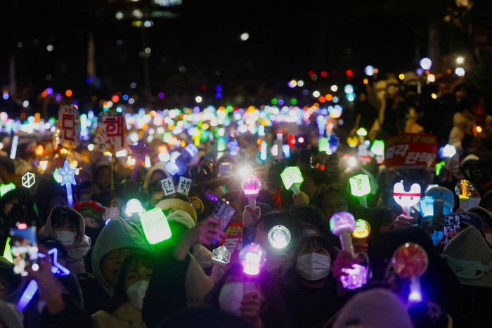 Ratusan penggemar K-pop di Korea Selatan ikut demo untuk mendesak pemakzulan Presiden Yoon Suk Yeol. Lightstick yang mereka bawa membuat suasana demo berwarna.