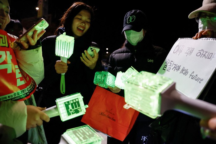 Ratusan penggemar K-pop di Korea Selatan ikut demo untuk mendesak pemakzulan Presiden Yoon Suk Yeol. Lightstick yang mereka bawa membuat suasana demo berwarna.