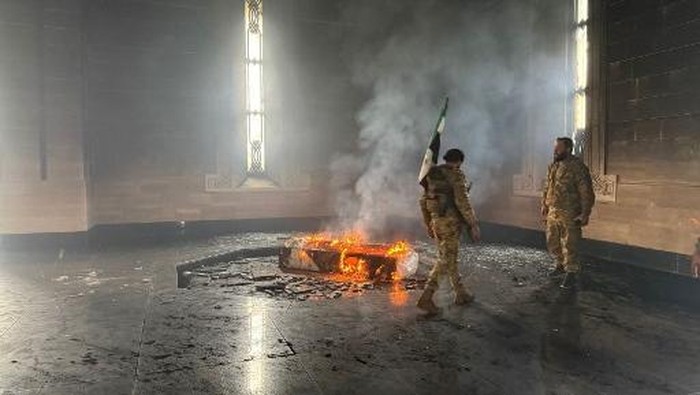 Rebel fighters stand next to the burning gravesite of Syrias late president Hafez al-Assad at his mausoleum in the familys ancestral village of Qardaha in the western Latakia province on December 11, 2024, after it was stormed by opposition factions. The father and predecessor of Syrias ousted president Bashar al-Assad died in 2000. (Photo by Aaref WATAD / AFP)