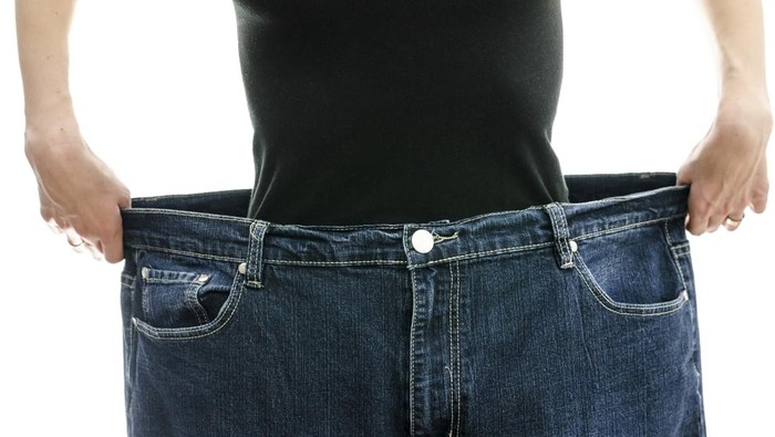 Woman showing how much weight she lost by wearing her old jeans. Weightloss concept.