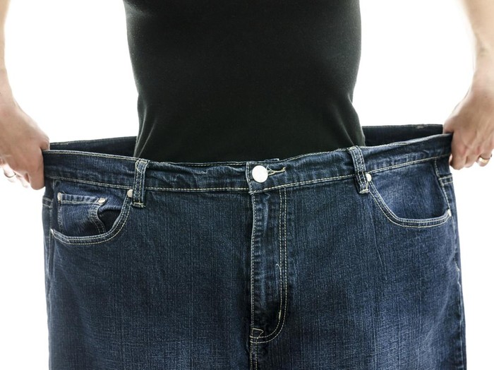 Woman showing how much weight she lost by wearing her old jeans. Weightloss concept.