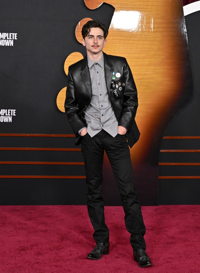 Aktor 28 tahun ini mengenakan blazer kulit hitam dengan aksen lencana dan pin yang memberi kesan edgy dan modern. Jas dipadukan dengan kemeja abu-abu berpotongan clean tanpa dasi, memberikan tampilan semi-formal yang tetap necis. Foto: Axelle/Bauer-Griffin/FilmMagic