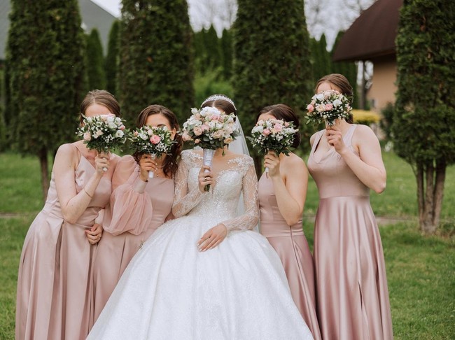 Group portrait of the bride and bridesmaids. Bride in a wedding dress and bridesmaids in pink or powder dresses and holding stylish bouquets on the wedding day.