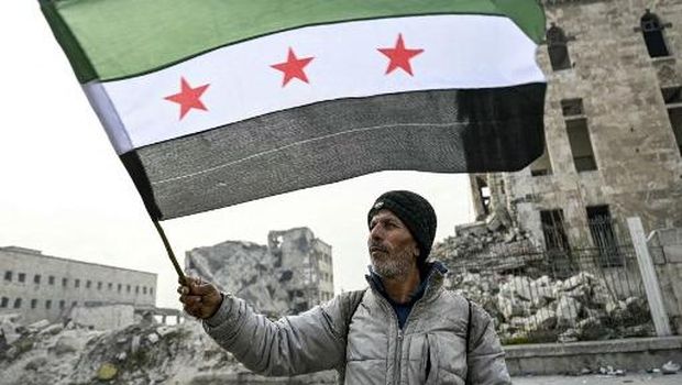 Seorang pria mengibarkan bendera oposisi Suriah di Benteng Aleppo di Suriah utara pada 11 Desember 2024. (Photo by Ozan KOSE / AFP)