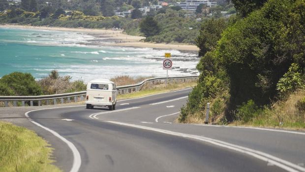 Volkswagen Kombi melewati Great Ocean Road dengan Pantai Lorne sebagai latar belakang.