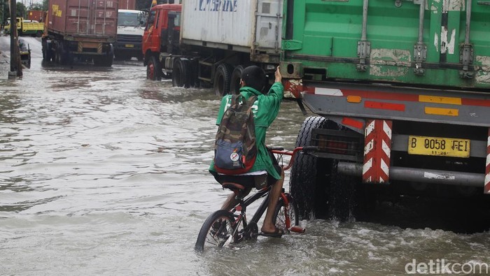 Truk kontainer menembus banjir air laut pasang (rob) di depan gerbang Pelabuhan Sunda Kelapa, Jl Lodan Raya, Jakarta Utara, Minggu (15/12/2024).