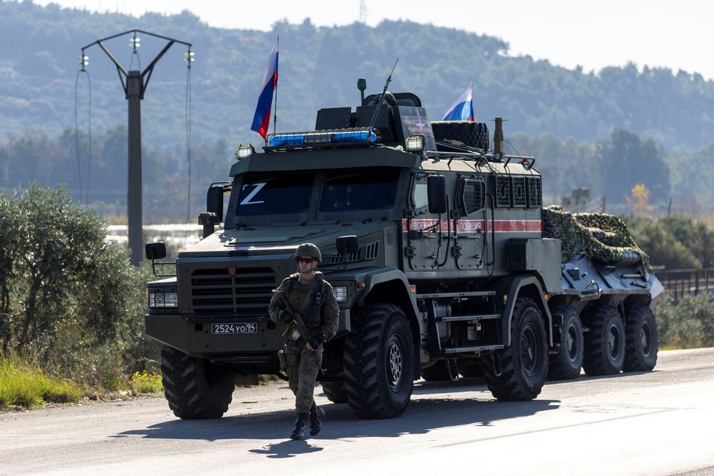 Seorang tentara Rusia berpatroli terhadap konvoi militer di pinggir jalan karena kerusakan mesin di salah satu kendaraan saat mereka melakukan perjalanan melalui pangkalan udara Hmeimim di wilayah pesisir Latakia, Suriah, 14 Desember 2024. (REUTERS/Umit Bektas)