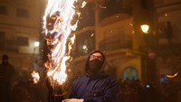 Para peserta festival membawa ranting-ranting pohon yang dibakar dan saling memukul kaki dengan cara yang unik dan penuh semangat.