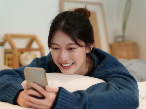Lifestyle concept. Happy young woman using cell phone on sofa at home.