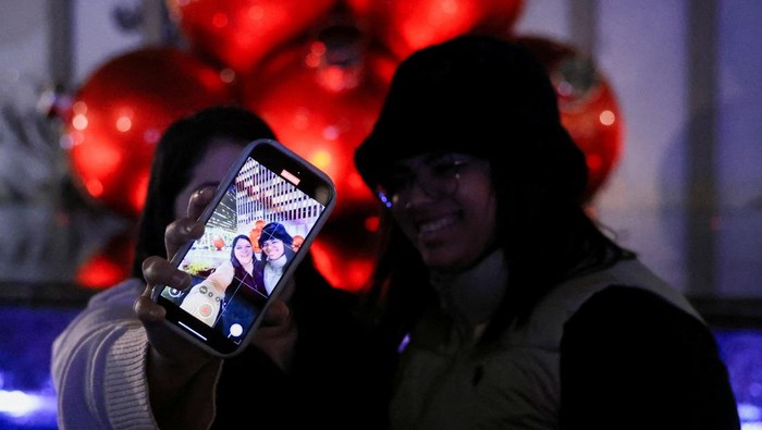 A tourist poses in Bryant Park in front of a Christmas tree, in New York City, New York U.S., December 9, 2024. REUTERS/Kent Edwards