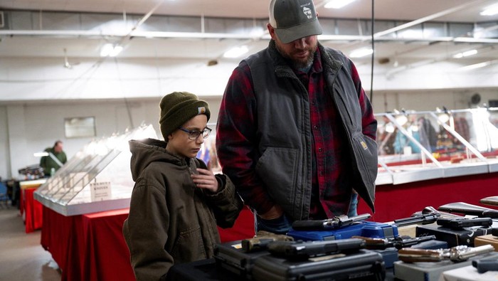 Jim Lierle, a vendor, holds a gun while speaking to a customer during the Peoria Gun & Knife Show in Peoria, Illinois, U.S. December 14, 2024.  REUTERS/Vincent Alban.  REFILE - CORRECTING TYPE OF WEAPON FROM 