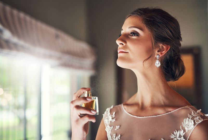 Potret studio seorang pengantin cantik memegang sebotol parfum.