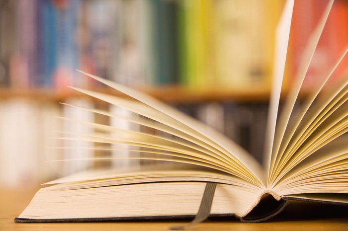 Sideview of an open book lying in front of bookshelf with books sorted in spectrum.