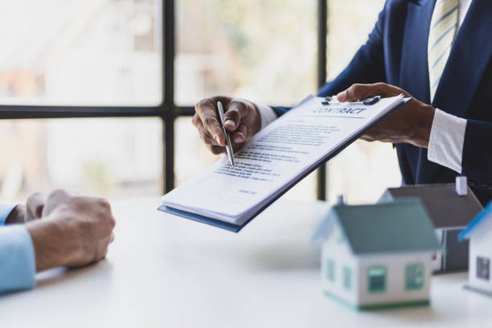 Businessman or lawyer uses pen to point at contract agreement document for client to sign.