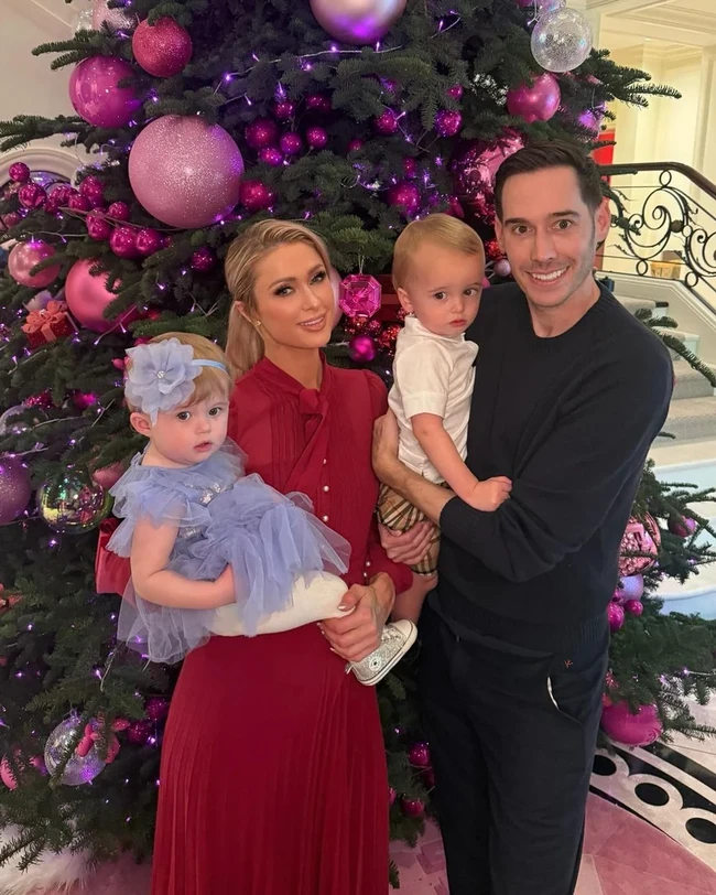 Paris Hilton memamerkan foto pohon Natal sekaligus kebersamaannya dengan suami, Carter Reum dan dua anaknya, Phoenix dan London. Mereka berpose dengan latar belakang pohon Natal yang didekor serba pink. Foto: Instagram