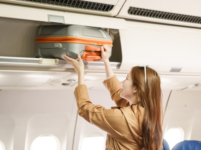 An Asian woman travels abroad by plane to study. She stands on the plane to collect her luggage, smiling and happy with the journey, excited about her new educational adventure.