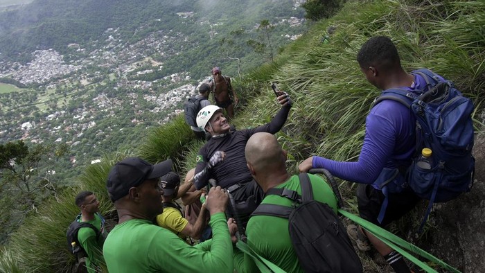 Semringahnya Atlet Disabilitas Diajak Panjat Tebing Brasil Ezequiel da Luz, a para-athlete with an amputated leg and no movement in his lower limbs, smiles in a wheelchair as he is taken on an inclusive route at Pedra da Gavea, with an organization that aims to increase accessibility in trails, in Rio de Janeiro, Wednesday, Dec. 18, 2024. (AP Photo/Lucas Dumphreys)