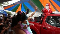 Petugas pemadam kebakaran berpakaian seperti Sinterklas menyapa anak-anak selama perayaan Natal di pantai Copacabana di Rio de Janeiro.
