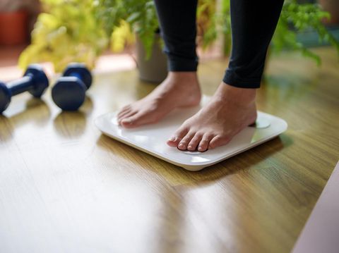 Ilustrasi diet atau timbangan berat badan A close-up view of a young woman standing on a weighing scale, focusing on her feet and the display as she checks her weight. The scene highlights the importance of health and self-awareness in maintaining a balanced lifestyle.