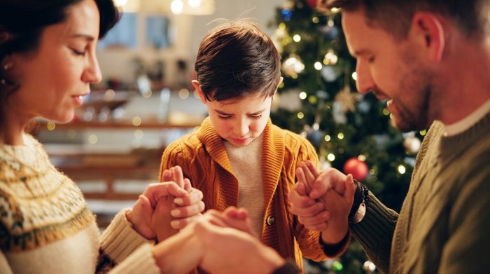 Family, prayer and holding hands in house for Christmas, solidarity and gratitude with spiritual connection. Parents, boy and worship in living room for thanks, faith and vacation as Christian people