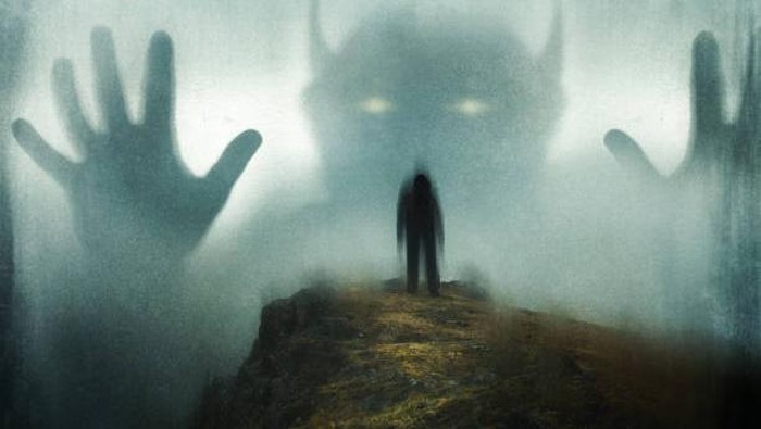 A man looking up at a huge ghostly horned demon appearing out the mist. On a moody day in the countryside. With a grunge, blurred edit.