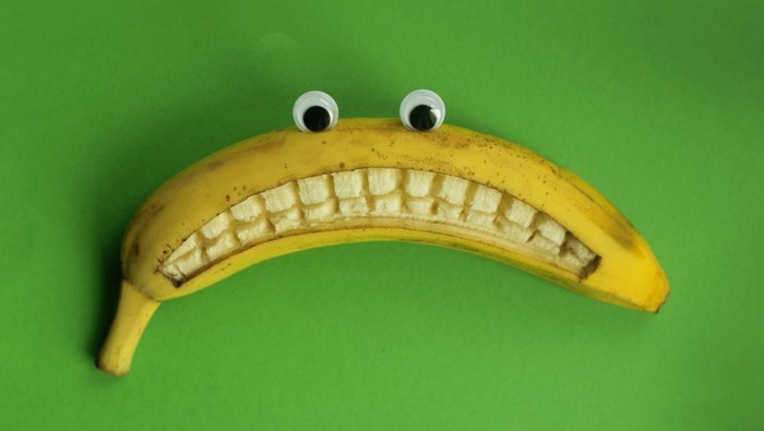 Banana with toy eyes and with a sad smile against a green background