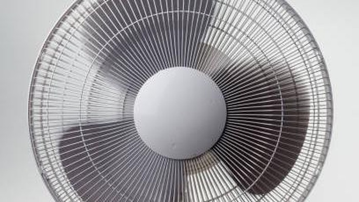 A pedestal fan turned on against a white background/wall