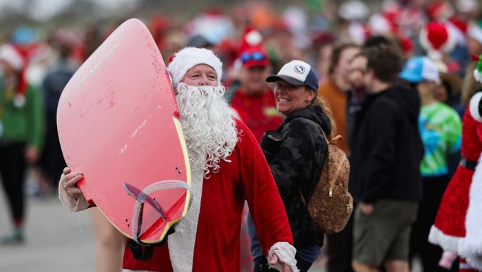 A surfer dressed as Santa places a plastic reindeer on the front of his board at the annual Surfing Santas Christmas Eve event in Cocoa Beach, Florida, U.S. December 24, 2024.  REUTERS/Sam Wolfe     TPX IMAGES OF THE DAY