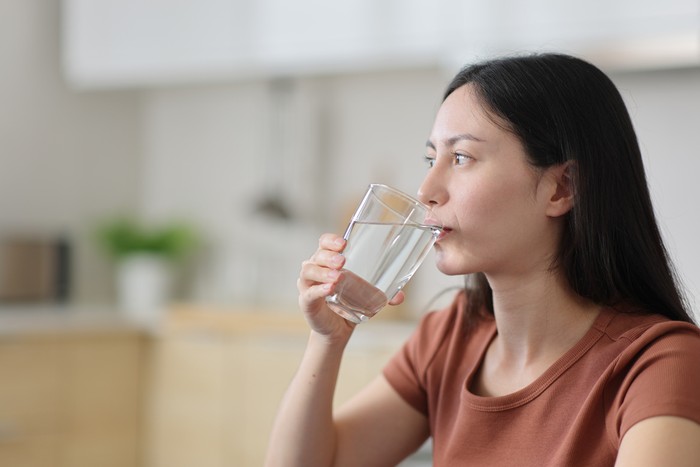 Asian woman drinking tap water from glass in the kitchen